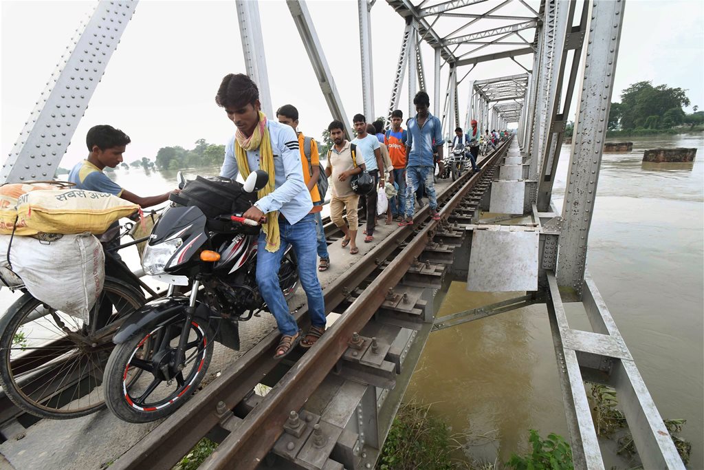 Chanpatia: Flood-affected people passing through a railway bridge at Chanpatia in West Champaran on Friday. PTI Photo(PTI8 18 2017 000116A)
