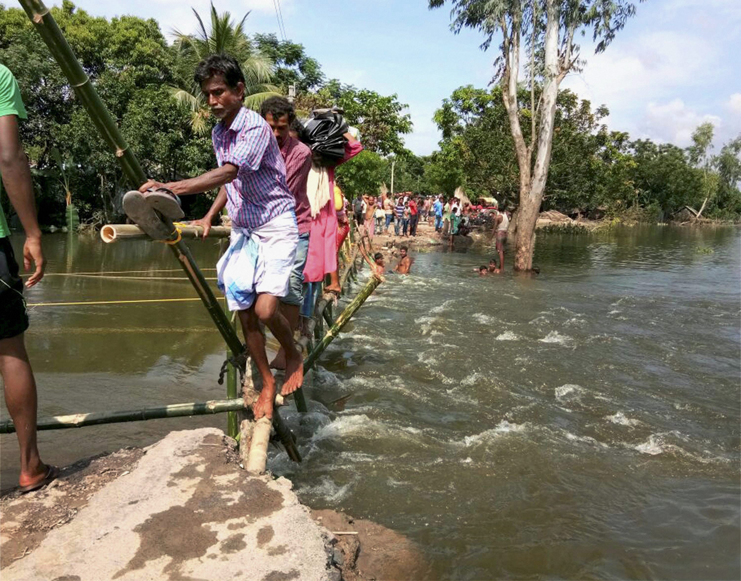 North Dinajpur: Villagers use a makeshift bamboo bridge to cross a flooded locality at Itahar village in North Dinajpur district of West Bengal on Sunday. PTI Photo (PTI8_21_2017_000113B)