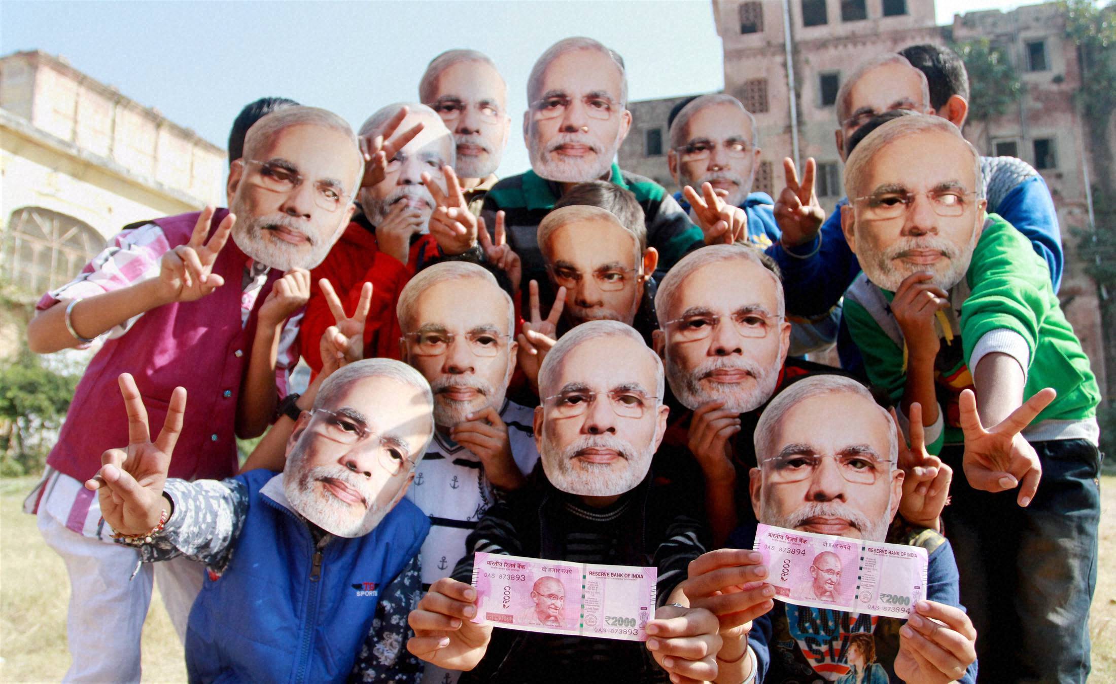 Jammu : Children wear Prime Minister Narendra Modi's mask and display new currency 2000 note as they welcome the demonetisation step in Jammu on Sunday. PTI Photo (PTI11_13_2016_000190B)