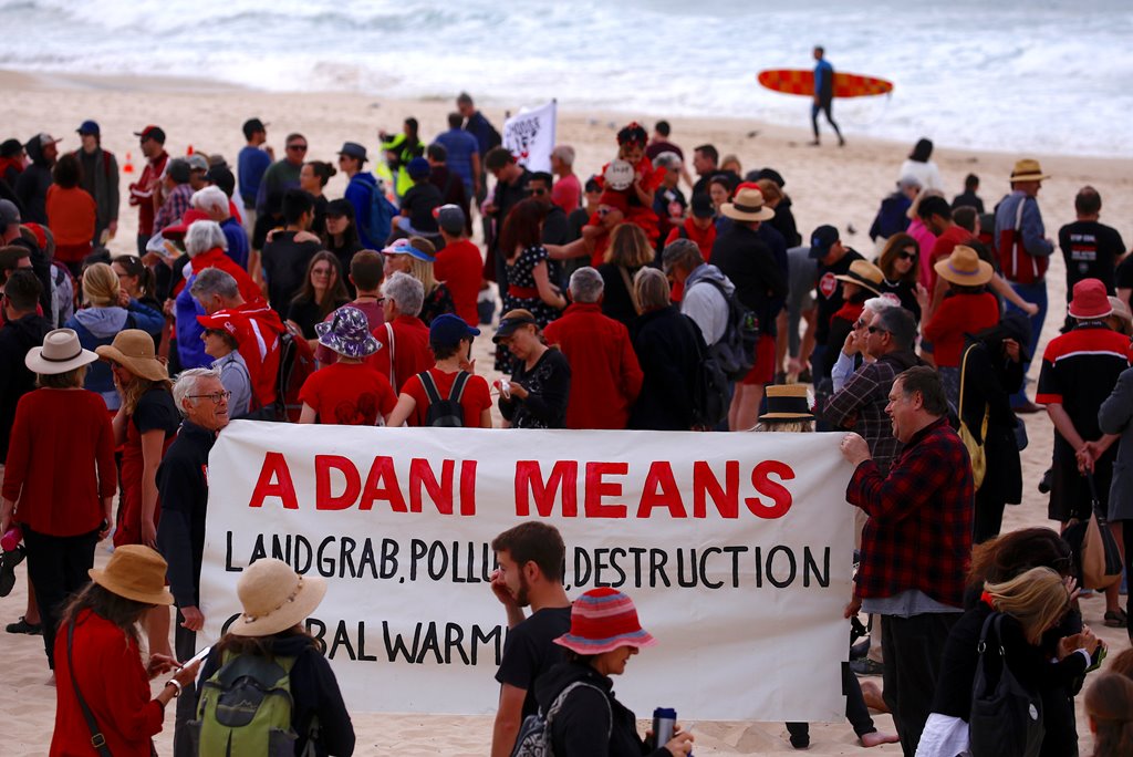 A surfer carries his board as he walks behind protesters participating in a national Day of Action against the Indian mining company Adani's planned coal mine project in north-east Australia, at Sydney's Bondi Beach in Australia, October 7, 2017. REUTERS/David Gray