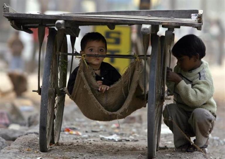 Children of slum dwellers play under a pushcart in New Delhi December 19, 2006. REUTERS/Ahmad Masood/Files