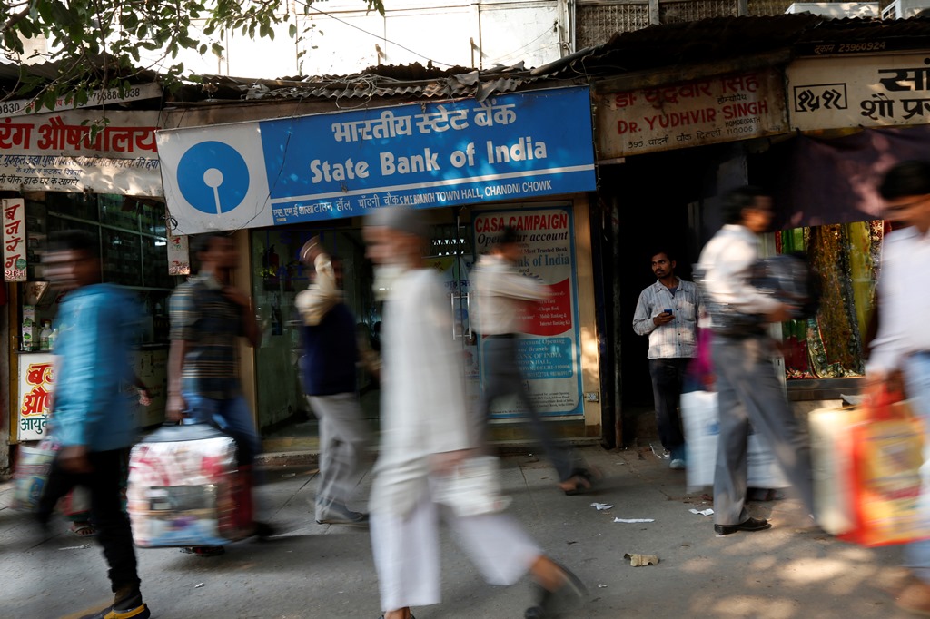 Commuters walk past a State Bank of India branch in the old quarters of Delhi November 13, 2013. State Bank of India (SBI) posted its steepest quarterly profit fall in more than two years as nonperforming loans increased, underlining the difficulties the bank's first chairwoman faces in keeping a lid on deteriorating assets. REUTERS/Mansi Thapliyal (INDIA - Tags: BUSINESS) - RTX15BLY