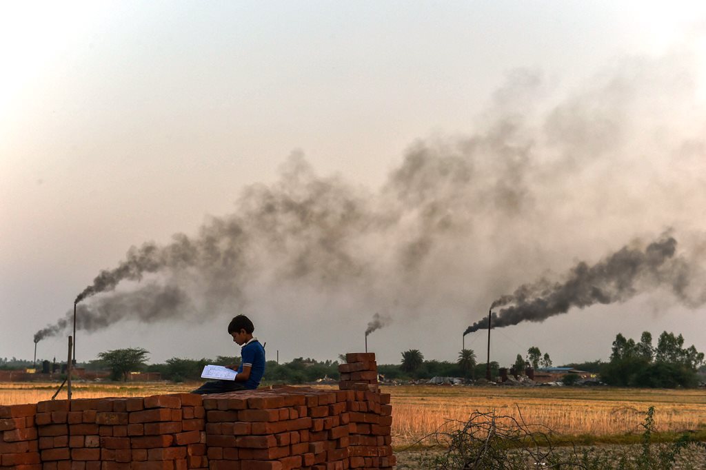 Kanpur: A child reads from a book, as thick black smoke rises in the sky from the glue factories at Dakari village of Unnao district near Kanpur on Friday. The World Health Organisation global air pollution database has revealed that India has 14 of the 20 most polluted cities in the world in terms of Particulate Matter (PM) 2.5 concentration, with Kanpur topping the charts. It said that nine out of 10 people in the world breathe air containing high levels of pollutants. PTI Photo by Arun Sharma(PTI5_6_2018_000146B)