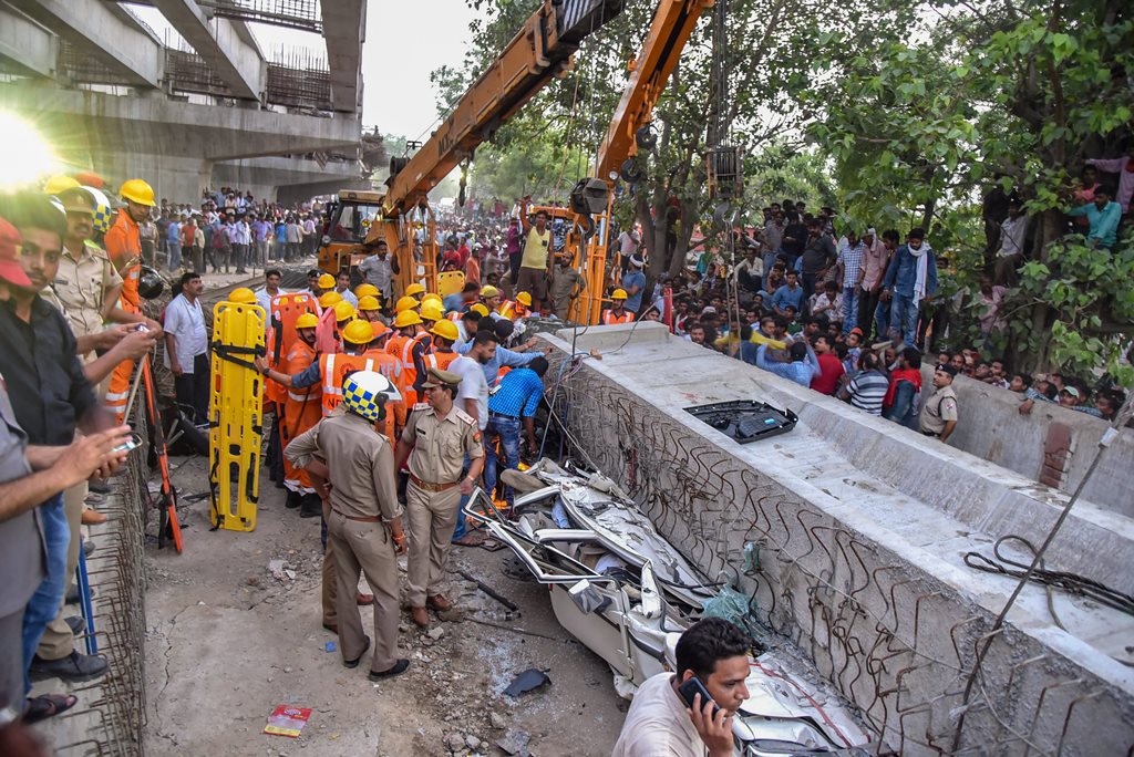 Varanasi: Locals and rescue teams gather near crushed vehicles after a portion of an under-construction flyover collapsed, leaving at least 12 dead, in Varanasi on Tuesday. (PTI Photo) (PTI5_15_2018_000164B)