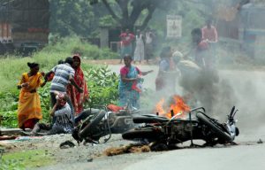 Nadia: People injured in poll violence sit by the side of a road as a vehicle is set on fire by locals during Panchayat polls, in Nadia district of West Bengal on Monday. (PTI Photo) (PTI5_14_2018_000125B)