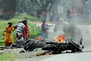 Nadia: People injured in poll violence sit by the side of a road as a vehicle is set on fire by locals during Panchayat polls, in Nadia district of West Bengal on Monday. (PTI Photo) (PTI5_14_2018_000125B)