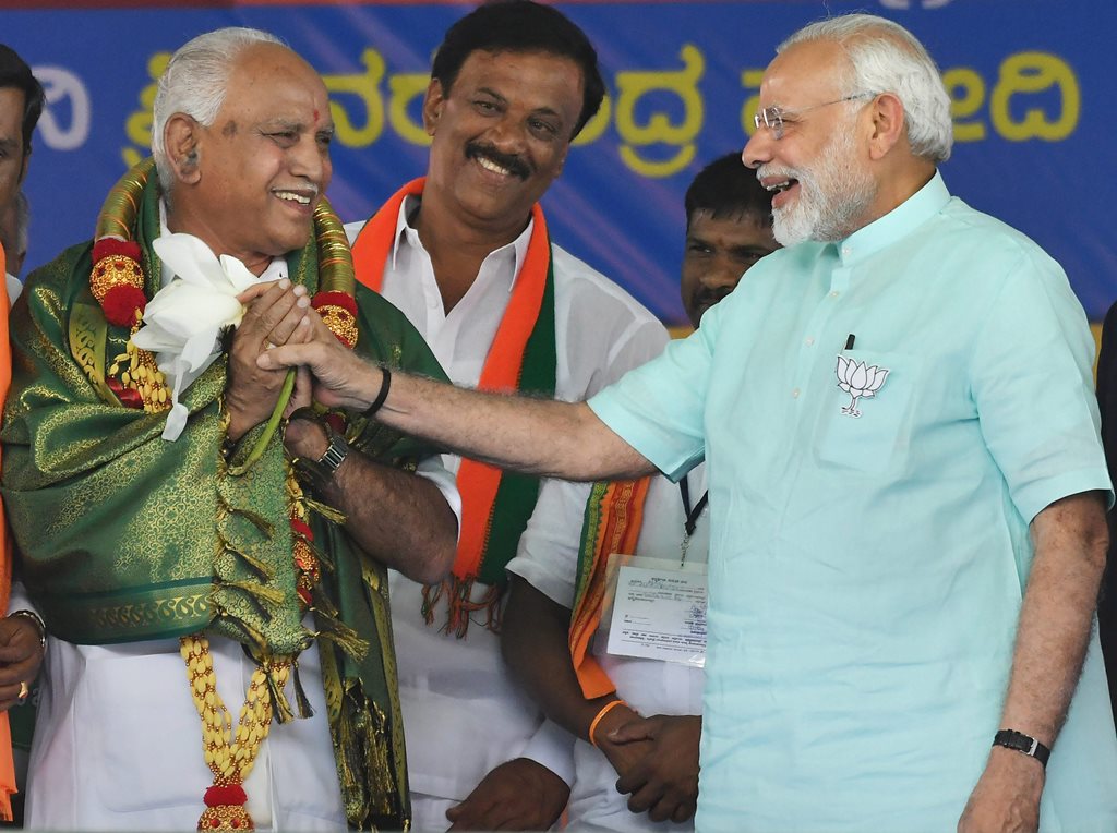 Chamarajanagar: Prime Minister Narendra Modi and BJP's chief ministerial candidate BS Yeddyurappa share a lighter moment during Karnataka election campaign rally at Chamarajanagar on Tuesday