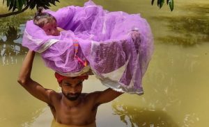 Sitamarhi: A man carries a child in a basket as he wades through a flooded street following incessant rainfall, in Sitamarhi, Friday, July 19, 2019. (PTI Photo)(PTI7_19_2019_000066B)