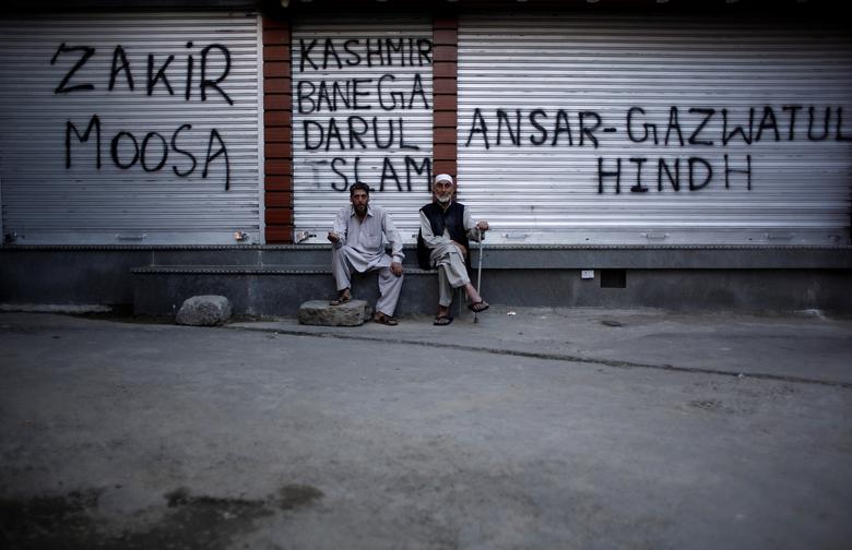 Kashmiri men sit in front of the closed shops painted with graffiti during restrictions after scrapping of the special constitutional status for Kashmir by the Indian government, in Srinagar, August 20, 2019. REUTERS/Adnan Abidi