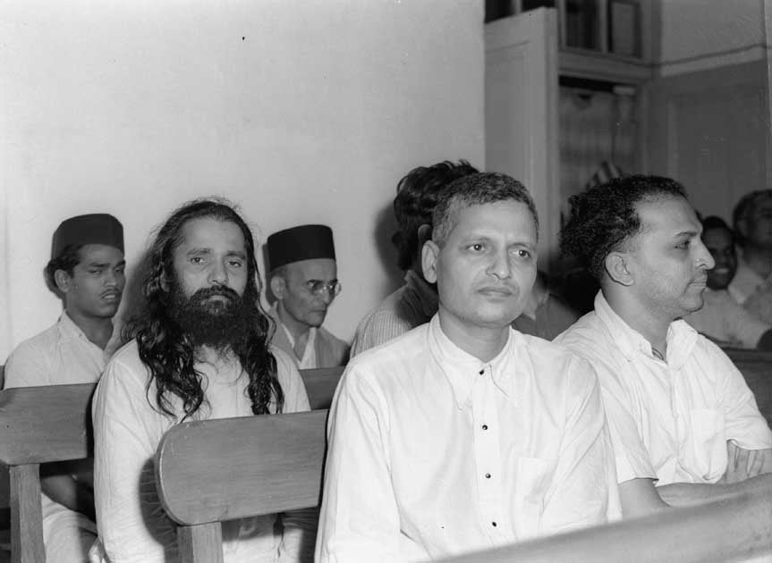 Photo taken during the trial of the persons accused of participation and complicity in Mahatma Gandhis assassination in a Special Court in Red Fort, Delhi. The trial began on May 27, 1948. V.D. Savarkar, wearing a black cap, is seated in the last row, while Nathuram Godse and Narayan Apte are up front. Credit: Photo Division, GOI