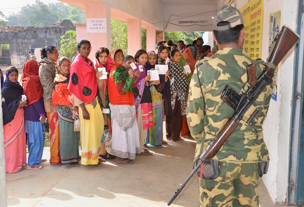 Bundu: A security jawan guards as people wait in queues to cast their votes at a polling station during the second phase of Jharkhand Assembly elections at Bundu, 45 kms from Ranchi, Saturday, Dec. 7, 2019. (PTI Photo) (PTI12_7_2019_000029B)