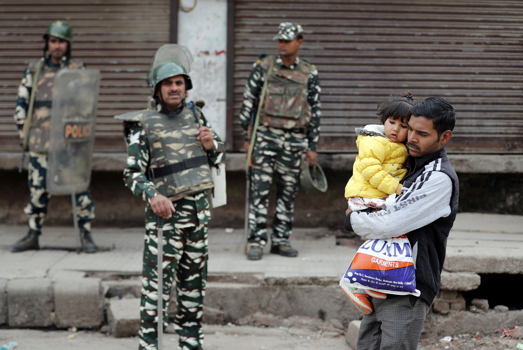 A man carrying a child walks past security forces in a riot affected area following clashes between people demonstrating for and against a new citizenship law in New Delhi, February 27, 2020. REUTERS/Adnan Abidi