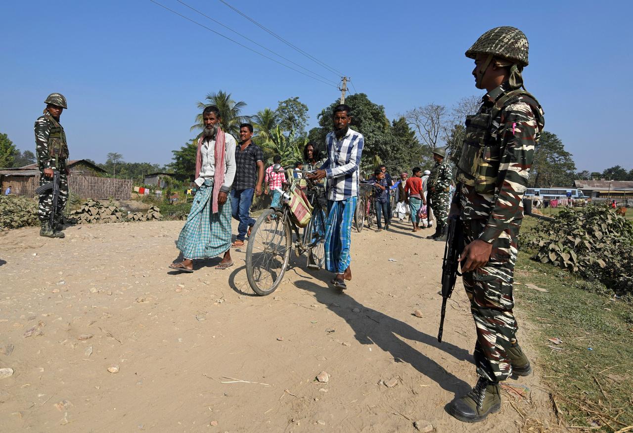 Villagers walk past Central Reserve Police Force (CRPF) personnel patrolling a road ahead of the publication of the first draft of the National Register of Citizens (NRC) in the Juria village of Nagaon district in the northeastern state of Assam, India, December 28, 2017. REUTERS/Anuwar Hazarika