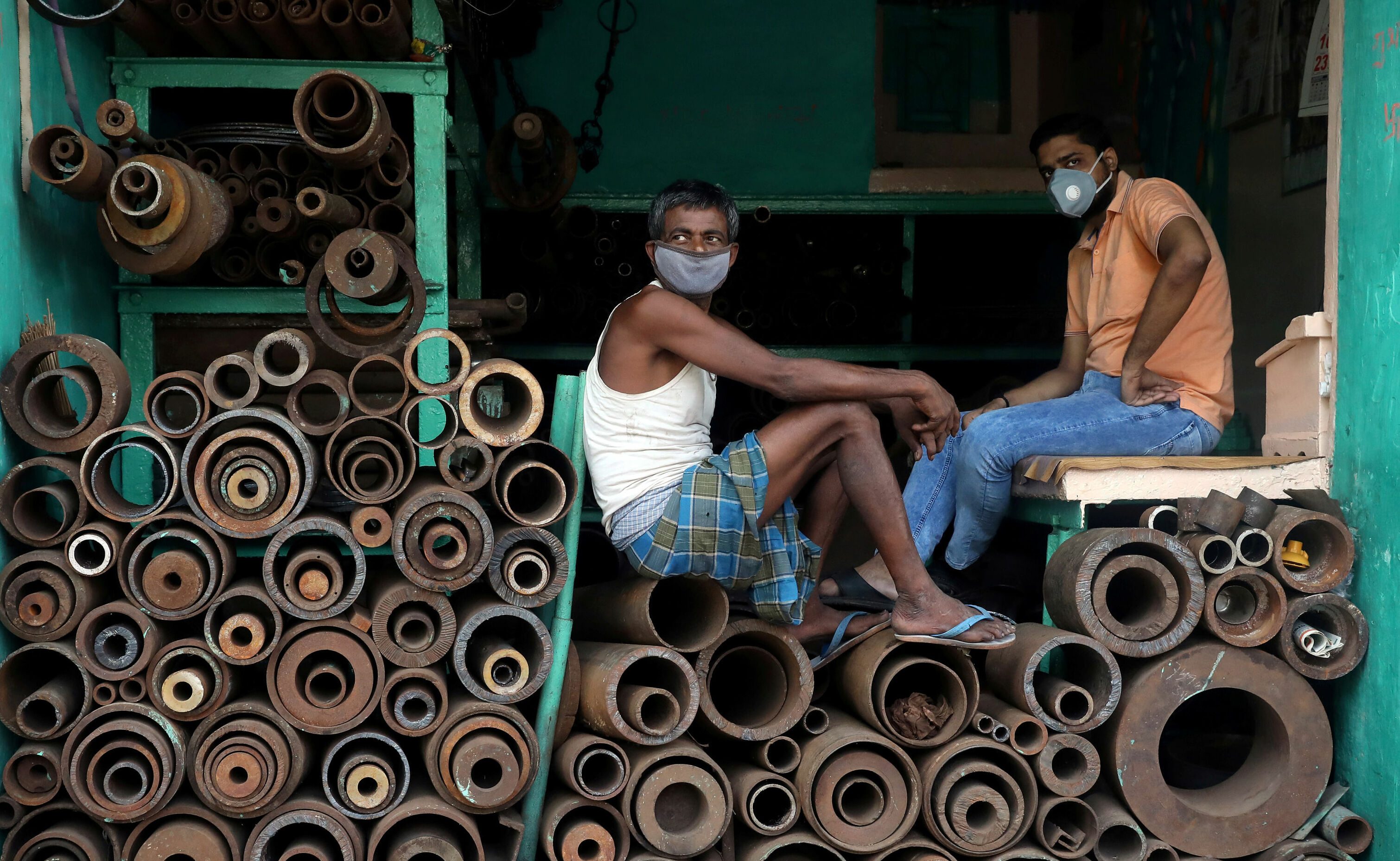 Workers wearing protective face masks sit inside a shop selling iron pipes at a wholesale iron market, after authorities eased lockdown restrictions that were imposed to slow the spread of the coronavirus disease (COVID-19), in Kolkata, India, June 15, 2020. Credit: Reuters 