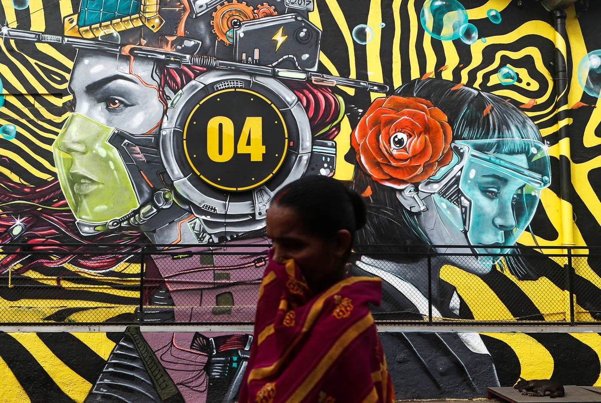 A woman walks past a graffiti of people wearing protective masks amidst the spread of the coronavirus disease (COVID-19), on the outskirts of Mumbai, India, December 9, 2020. REUTERS/Francis Mascarenhas/Files