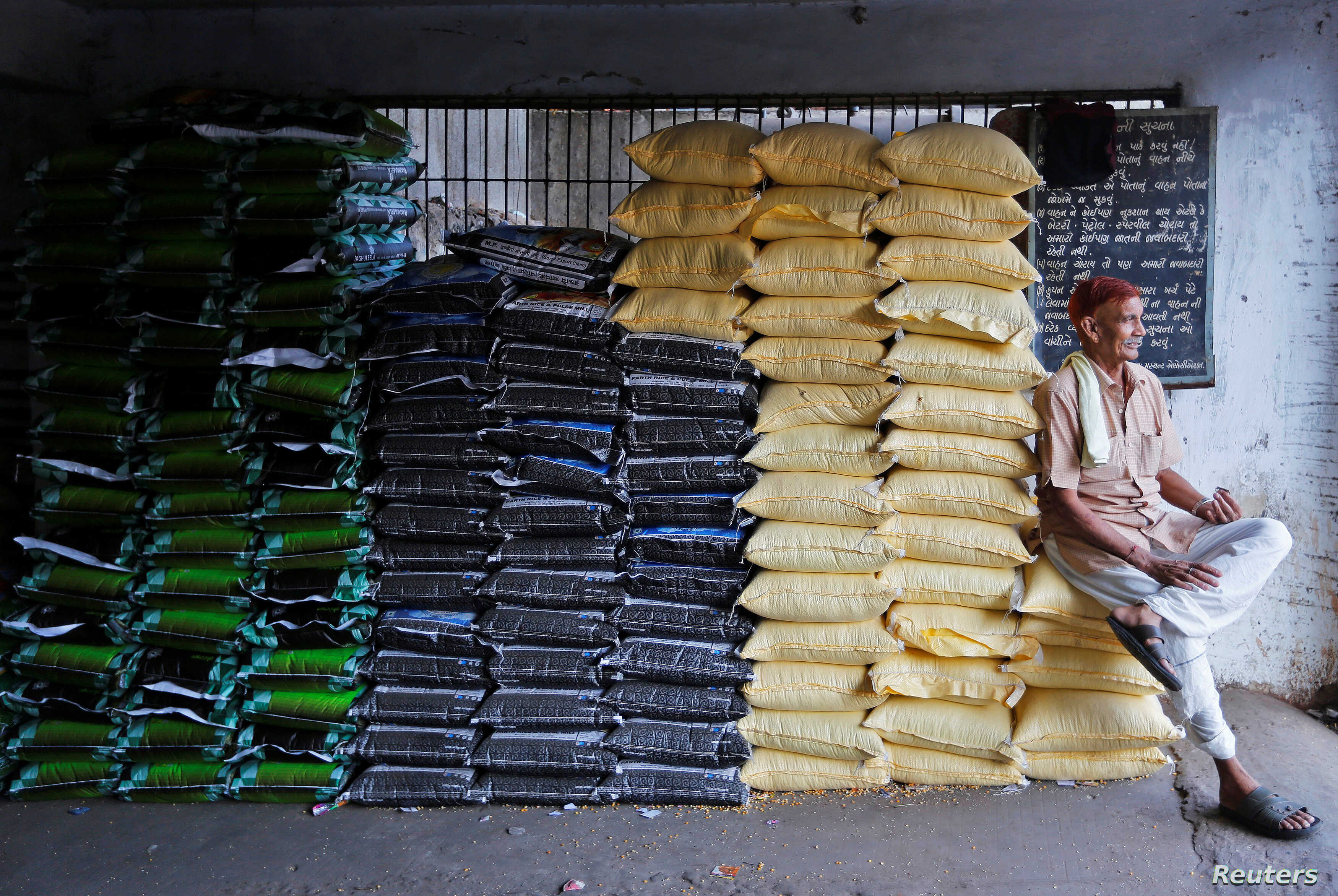 A labourer sits on sacks of food grains while waiting for customers at a wholesale market in Ahmedabad, India, December 14, 2016. REUTERS/Amit Dave - RTX2UXYK