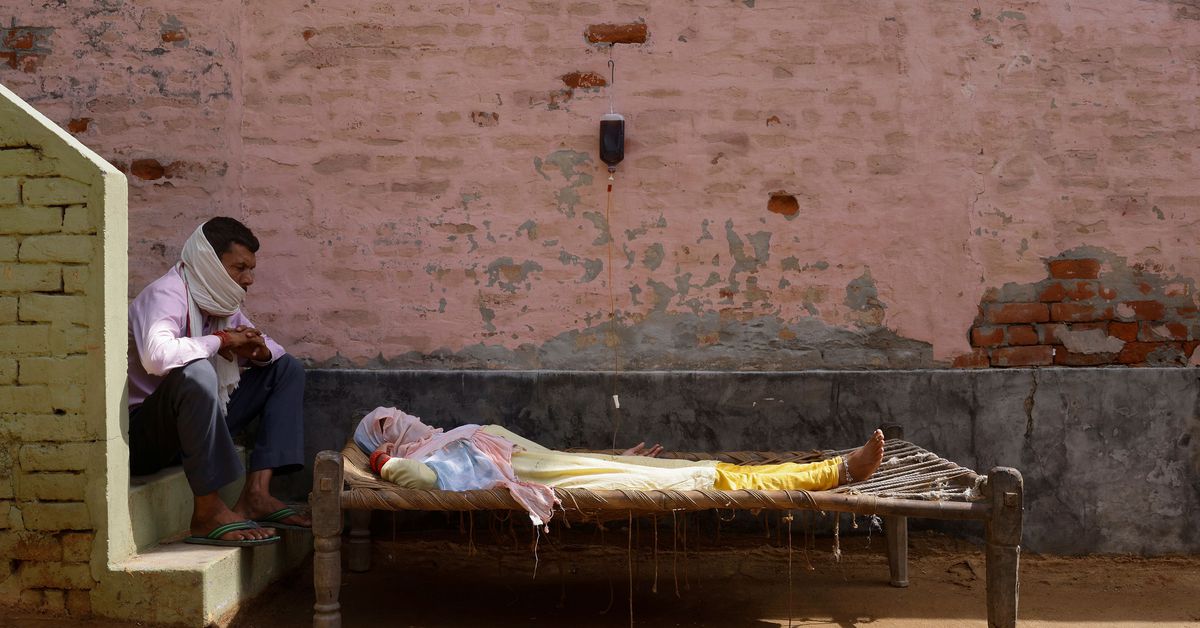 A man sits next to his wife, who is suffering from fever as she receives treatment at a clinic set up by a local villager, amidst the spread of the coronavirus disease (COVID-19), in Parsaul village in Greater Noida, in the northern state of Uttar Pradesh, India, May 22, 2021. REUTERS/Adnan Abidi 